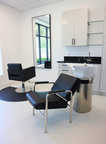 Hair salon interior with a black chair, wash station, large mirror, and white walls