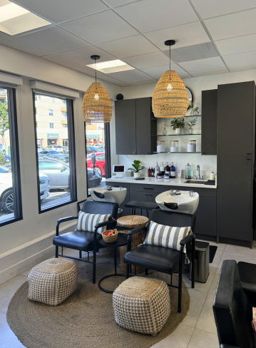 Interior of a salon with two chairs, a sink, shelves, and pendant lighting