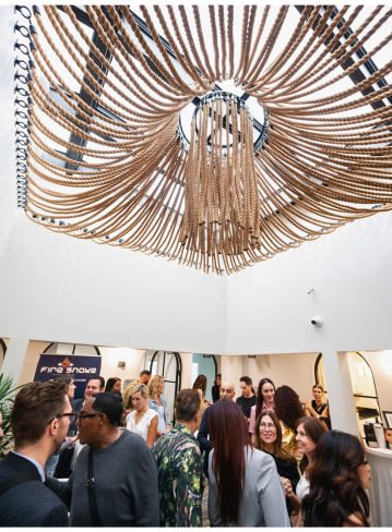 A group of people gathers under a circular rope chandelier in a well-lit space