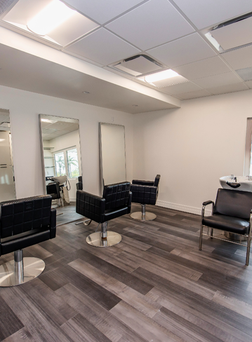 Interior of a hair salon with three styling chairs and mirrors, wooden flooring, and bright lighting
