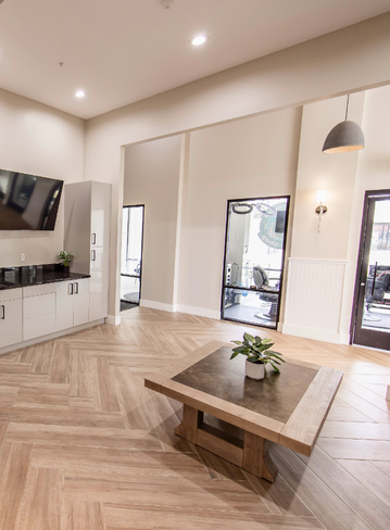 Interior room with a wooden table, laminated flooring, and a kitchenette. Windows on two walls