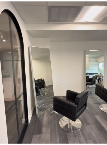 A modern salon interior with black chairs and mirrors, featuring white walls and gray flooring