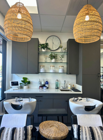 Interior of a salon with two sinks, cabinets, plants, and woven pendant lights