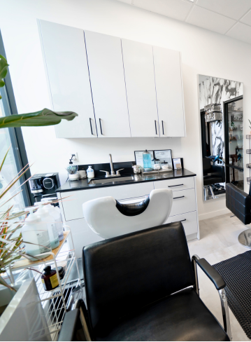 Interior of a salon with a black chair, mirrored wall, and white cabinets