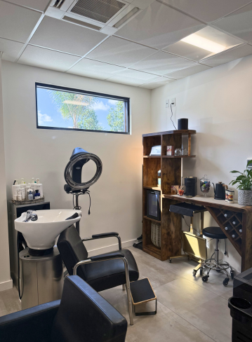 A salon interior with a shampoo station, chairs, and a wooden shelf with products