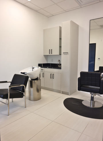 Interior of a salon with chairs, a sink, storage cabinets, and a circular rug