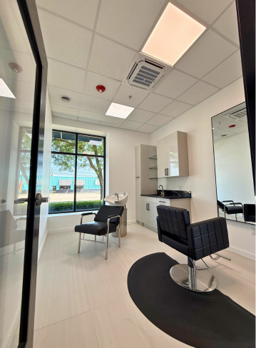 Interior of a hair salon with two chairs, a mirror, and large windows