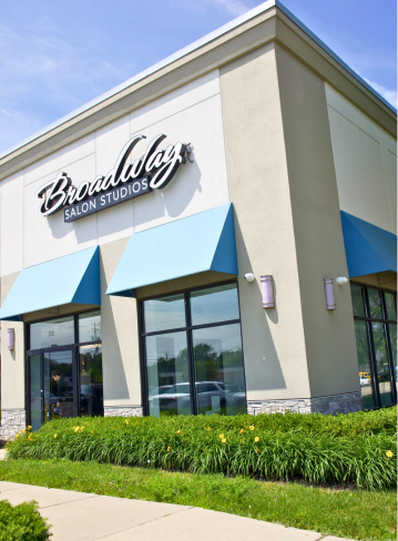 Exterior of a salon building with blue awnings and green landscaping