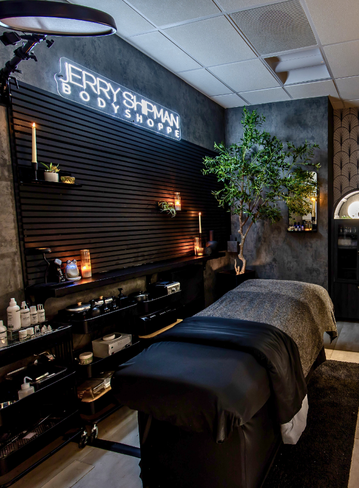 Spa treatment room with a massage table, plants, candles, and wall shelves