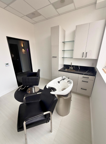Interior view of a salon with two chairs, a sink, and storage cabinets