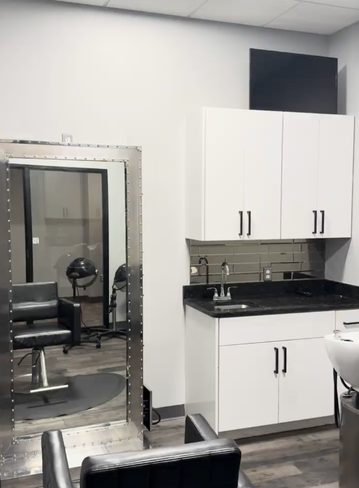 A modern salon interior with a mirror, sink, cabinets, and two chairs