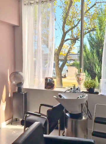 Hair salon interior with a basin, black chairs, and large windows. Trees visible outside