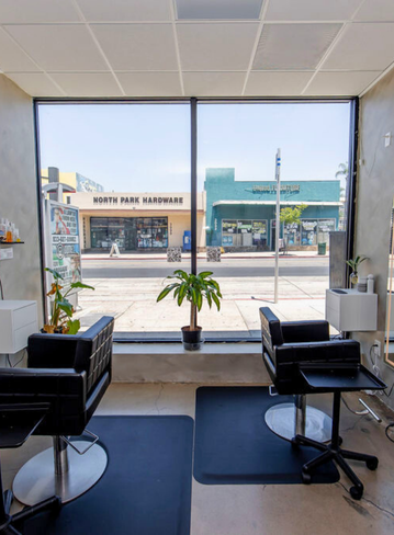 Interior of a salon with two chairs facing a large window showing a street view