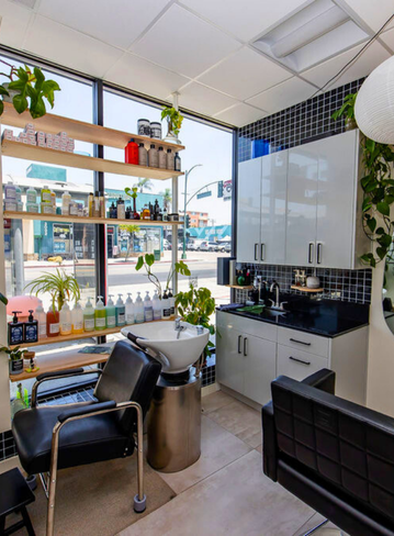Interior of a salon with shelves of products, sink, and styling chairs by large windows