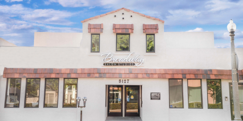 White building with a peaked roof, multiple windows, and a sign above the entrance