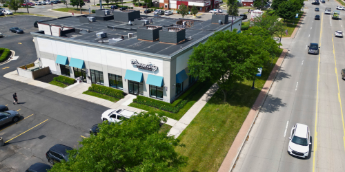 Aerial view of a commercial building near a road with parking and trees