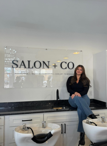 A woman sitting on a counter in front of a sign that says "SALON + CO."