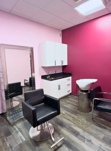 Interior of a salon with a black chair, mirror, cabinet, and a wash station. Pink and purple walls