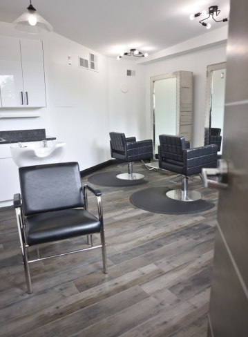 A modern hair salon with black chairs, mirrors, and a sink area. Wood flooring