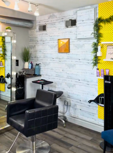 Interior of a salon with a black chair, mirror, and yellow wall with products