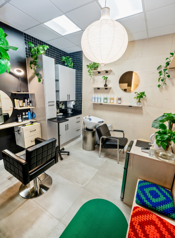 Interior of a salon with styling chair, mirrors, plants, and a light fixture