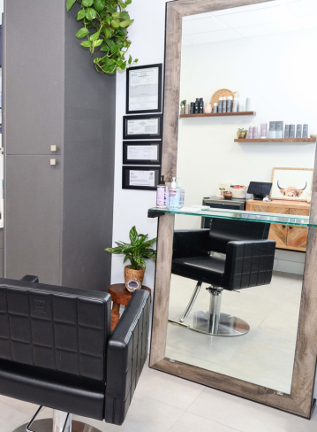 Hair salon interior with a black chair, mirror, plants, and shelves of products