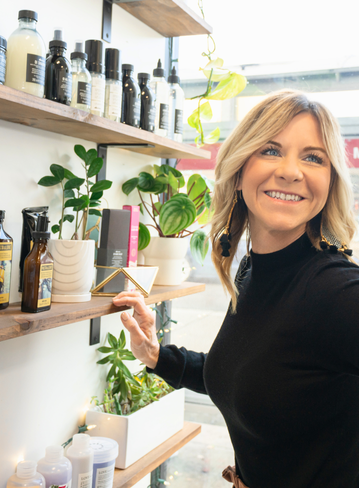 Person smiling while standing next to shelves with various bottles and plants