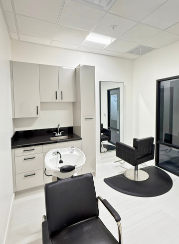 A hair salon interior with a sink, mirror, chair, and cabinetry in a light room