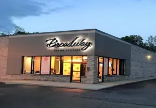 Exterior of a salon building at dusk with large windows and a sign on the wall