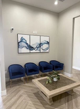A waiting area with four blue chairs, a table, and abstract wall art