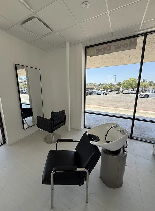 Interior of a salon with a mirror, black chair, and sink near a large window