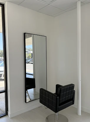 A black salon chair next to a tall, rectangular mirror on a white wall