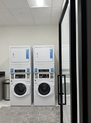 Two stacked laundry machines in a room with a trash can and glass door