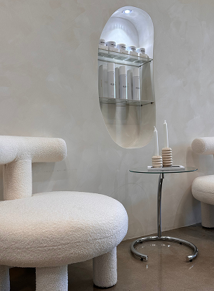 Two white plush chairs next to a glass side table with candles and a display shelf