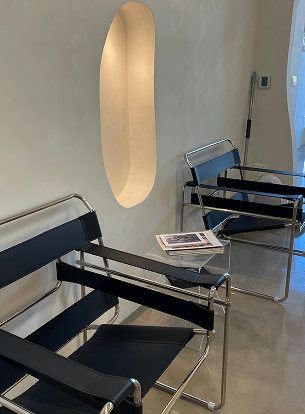 Two modern chairs with black upholstery next to a wall with an oval cutout. A magazine rests on a ta