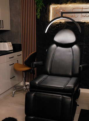 Black aesthetic treatment chair with a light above, set in a modern clinic interior