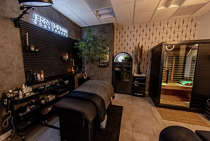 Interior of a spa room with a massage table, plants, and a sauna
