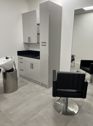 A modern salon interior with a black chair, sink, and cabinets. A mirror is visible