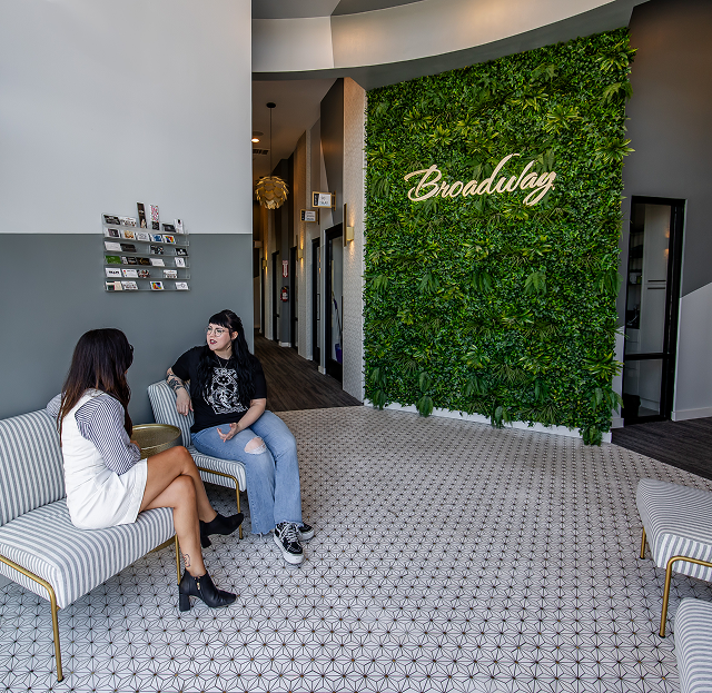 Two people sitting on a bench in a lobby with a green wall and patterned floor
