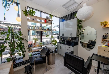 A salon interior with shelves, a mirror, chairs, and plants by large windows
